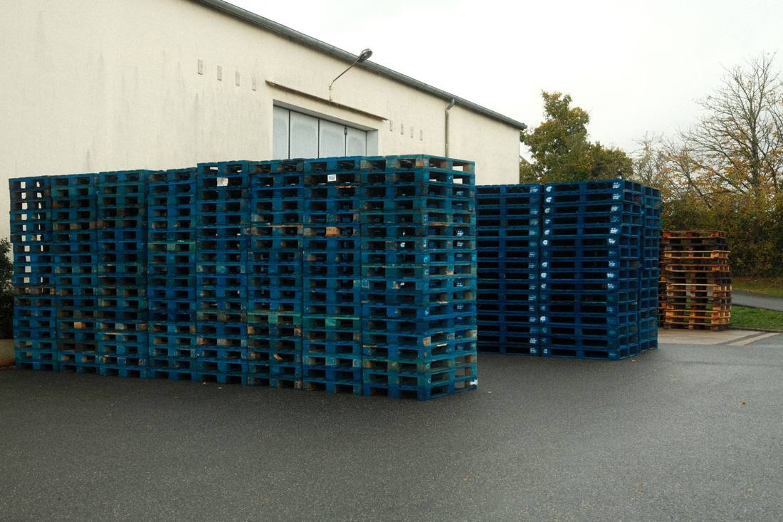 Massive stack of blue wooden pallets outside a building, ready for transport.